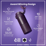A dark-purple, double-walled stainless steel thermos is being held. It features a hide-away carry handle, crevice-free design, hygiene cover, and wide mouth. The thermos keeps beverages hot or cold longer and is an award-winning design.